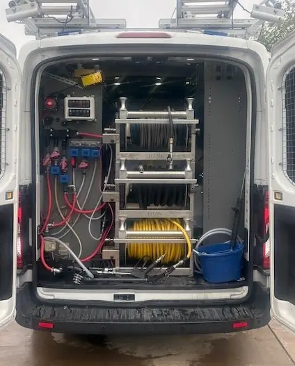 Interior of a custom-built soft-wash van showing hose reels, manifolds, and control panel